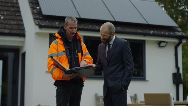  Businessman & engineer discuss solar panels on roof at residential property
