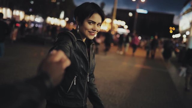 Slowmotion of woman follow me holding male hand looking to camera at night time