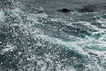 Naklejka premium Boiling surface of water under the influence of strong wind. Splashes and drops of water scatter in different directions. Cold cyan water background.