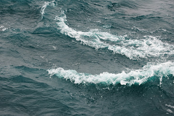 Boiling surface of water under the influence of strong wind. Splashes and drops of water scatter in different directions. Cold cyan water background.