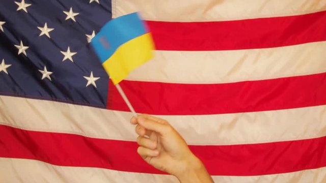 Ukrainian flag against the background of the American flag. A small Ukrainian flag and a large US flag.