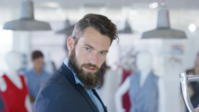 Male customer trying on suit and looking into mirror in fashion clothing store. Seen from mirror's pov with other customer's shopping in background.