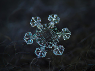 Real snowflake at high magnification. Macro photo of large star plate snow crystal with short, broad arms and unusual pattern inside central hexagon. Snowflake glowing on dark gray textured background