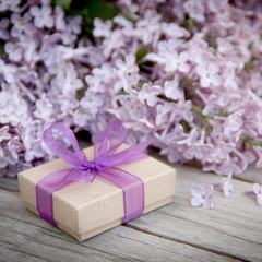 Fototapeta na wymiar Gift box with purple bow and lilac on wood