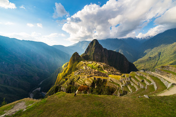 Machu Picchu beleuchtet vom warmen Sonnenuntergangslicht. Weitwinkelansicht von den Terrassen oben mit malerischem Himmel und Sonne platzen. Traumhaftes Reiseziel, Weltwunder. Cusco-Region, Peru.