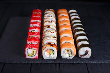 Tasty appetizing  multicolored maki sushi rolls set with wide assortment of fillings, served on black stone slate. Restaurant menu