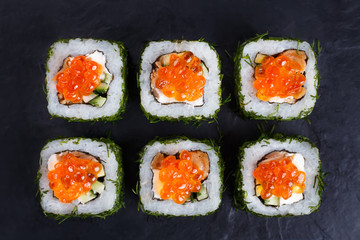 Japanese food, sushi restaurant. Delicious sushi rolls topped with caviar in chopped dill served on black slate, flat lay