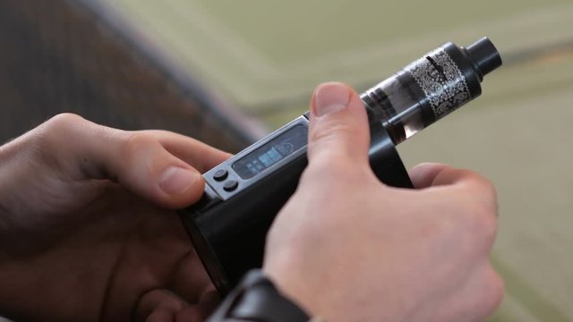 a man holds an electronic cigarette in his hand and enters the necessary settings