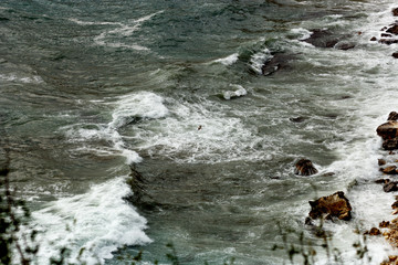 A seagull is flying over white foam of waves and is fishing on the beach during a storm. A dramatic image under a strong storm with large waves. View from above.