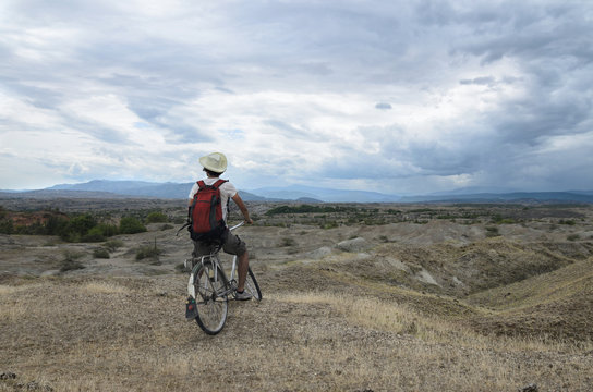 Back view of a traveler on a bicycle overlooking stunning prairie and mountains landscape