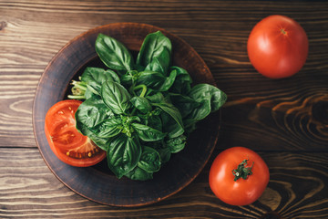 Top view on a brown wooden table with tomatoes and plate with green basil
