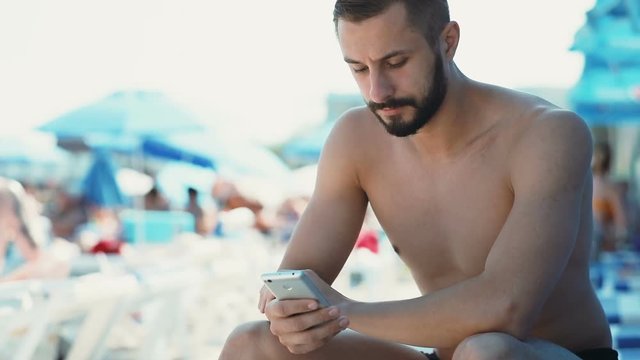 Modern technology portrait young attractive man caucasian holding smart phone mobile sea beach summer holidays blurred background naked guy bearded internet surfing reading leisure calm serious face