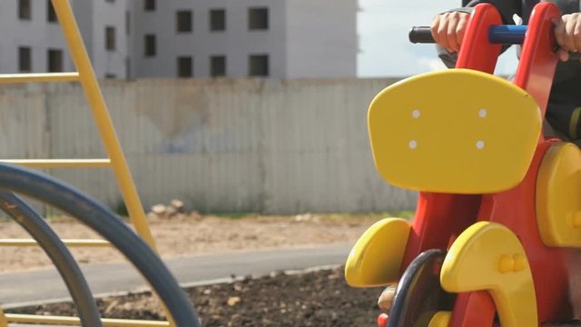 Unknown little boy in snickers ride swing in the form of horse in the courtyard of new micro district in the city outdoors