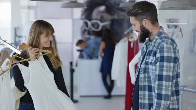 Cheerful couple shopping together, looking at clothes in boutique clothing store.