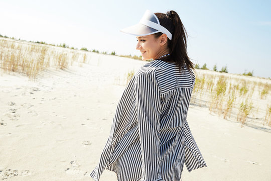 A Girl Walking In A Black And White Stripes Shirt And A Visor Hat Around A Beach Enjoying The Sun