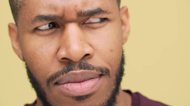 extreme closeup thoughtful metis man with hazel eyes wearing sporty clothes looking at camera with frown expressing mixed emotions looking side to side over yellow background. Concept of emotions