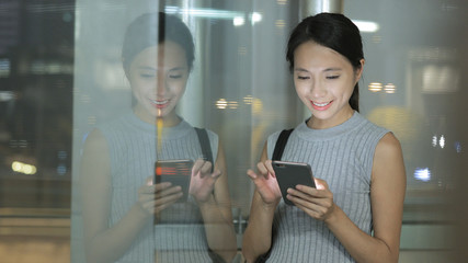 Window reflection of woman using smart phone at night