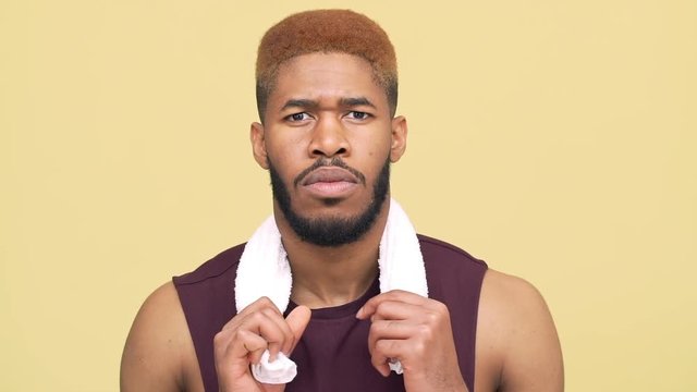 sporty metis guy with stylish haircut wearing workout clothes taking break after training putting white towel over neck isolated over yellow background closeup slow motion