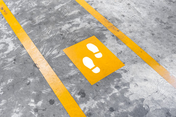Walkway lane in parking building. Painted yellow footsteps between parallel yellow lines on abstract cement floor.
