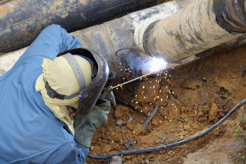 Worker welder pipe arc welding for connection water supply at construction site.