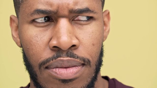 slomo extreme closeup thoughtful metis man with hazel eyes wearing sporty clothes looking at camera with frown expressing mixed emotions looking side to side over yellow background. Concept of