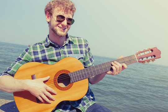 Young man hipster playing guitar by sea ocean.