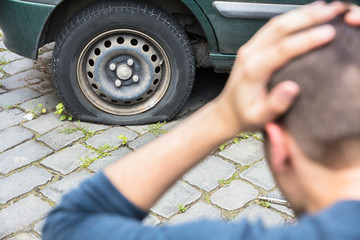 Worried Man Looking At Punctured Car Tire