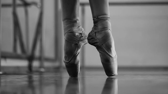 Ballerina in ballet pointe stretches on barre in gym. Slow motion. Woman practicing in dance studio. Work out of young girl. Black and white footage.