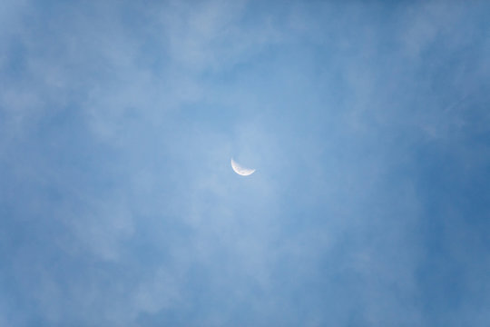 Small moon in the center photo with blue sky and behind little clouds.