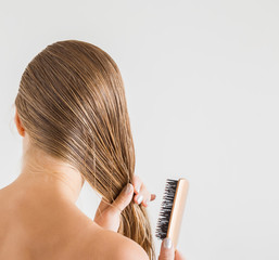 Woman with comb brushing her wet blonde hair after shower on the gray background. Cares about a healthy and clean hair. Beauty salon concept.