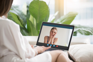 Casual girl talks to laughing girlfriend via video conference application. Woman makes call to female friend on laptop. Long distance friendship, virtual communication. Close up view, focus on screen.