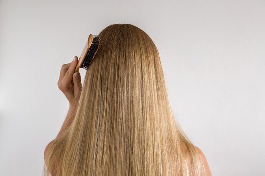 Woman with comb brushing her dry blonde hair on the gray background. Cares about a healthy and clean hair. Beauty salon concept.