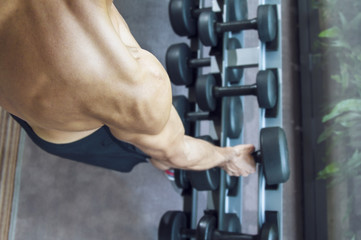 Young handsome muscular man exercising in the gym. Picking dumbbell from weight rack.