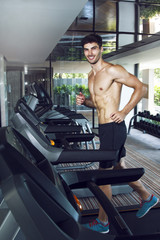 Fototapeta na wymiar Young healthy handsome man training in the gym on the treadmill. Running with smile and without t-shirt. 