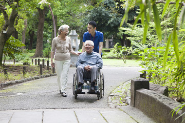 An old couple walking in the park with help from care workers