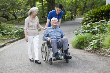 An old couple walking in the park with help from care workers