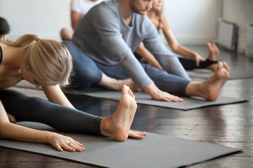 Fototapeten Junge sportliche Menschen praktizieren Yoga-Unterricht mit Lehrer, sitzen in Janu Sirsasana-Übung, Kopf-zu-Knie-Vorwärtsbeuge-Pose, trainieren, Innen-Nahaufnahme, Studio. Wohlbefinden, Wellnesskonzept © fizkes