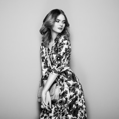 Fototapeta premium Blonde Young Woman in Floral Spring Summer Dress. Girl posing on a White Background. Stylish Wavy Hairstyle. Fashion photo. Glamour Lady with Handbag. Black and White photo