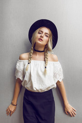 Close up of beautiful young blonde woman with black hat. Her hair is tied in two big ponytails. Around neck she has black choker.