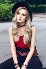Close up of beautiful young blonde woman with black hat She is wearing red tshirt, around neck she has black choker and on hands many bracelets.