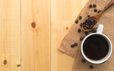 A cup of coffee and coffee bean grain on sack fabric put on pine wood table background include copyspace for add text or graphic