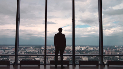 Fototapeta na wymiar Rear view of businessman in an office with panoramic city view. Businessman admires the city from the panoramic Windows in the city centre