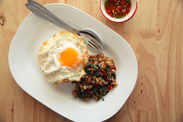 stir fried pork and basil with rice and egg on wood background thai food