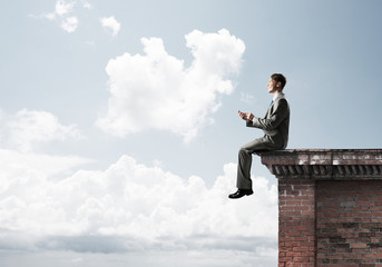 Man on roof edge reading book and cityscape at background