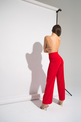 Beautiful Naked Woman With Perfect Body In Red Pants Posing Casting Shadow Isolated On The Gray Background