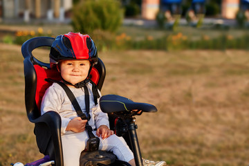 Fototapeta na wymiar Little girl in red and black helmet seat bicycle in city park