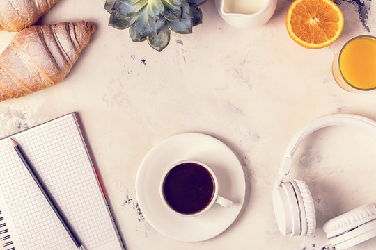 Notepad, headphones, croissants and coffee on white table.