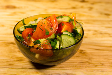 Fresh salad with tomato, cucumber, onion, parsley and dill in glass bowl on wooden table