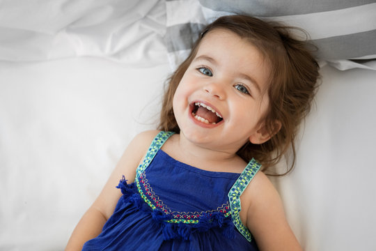 portrait of a smiling toddler girl lying on bed