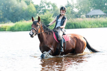 Fototapeta premium Smililng young teenage girl riding horseback in river